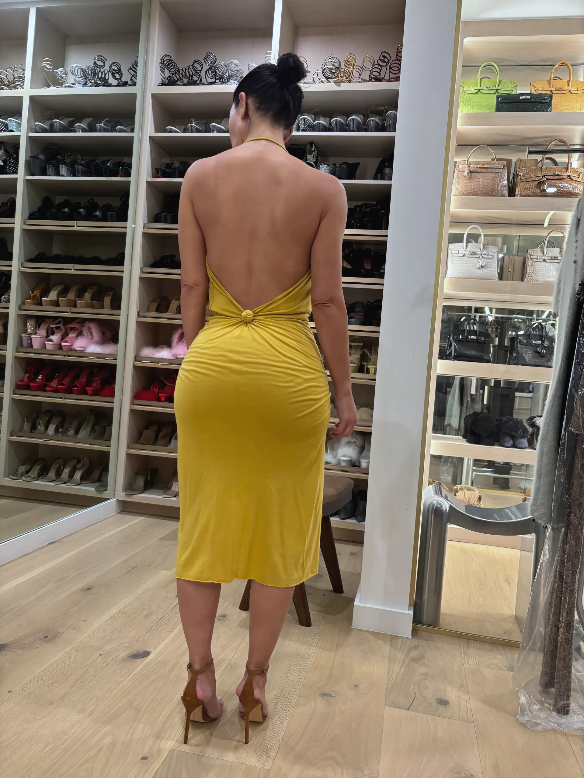 Yellow jersey halter dress with a deep open back and knotted detail at the waist, rear view, worn in a dressing room.