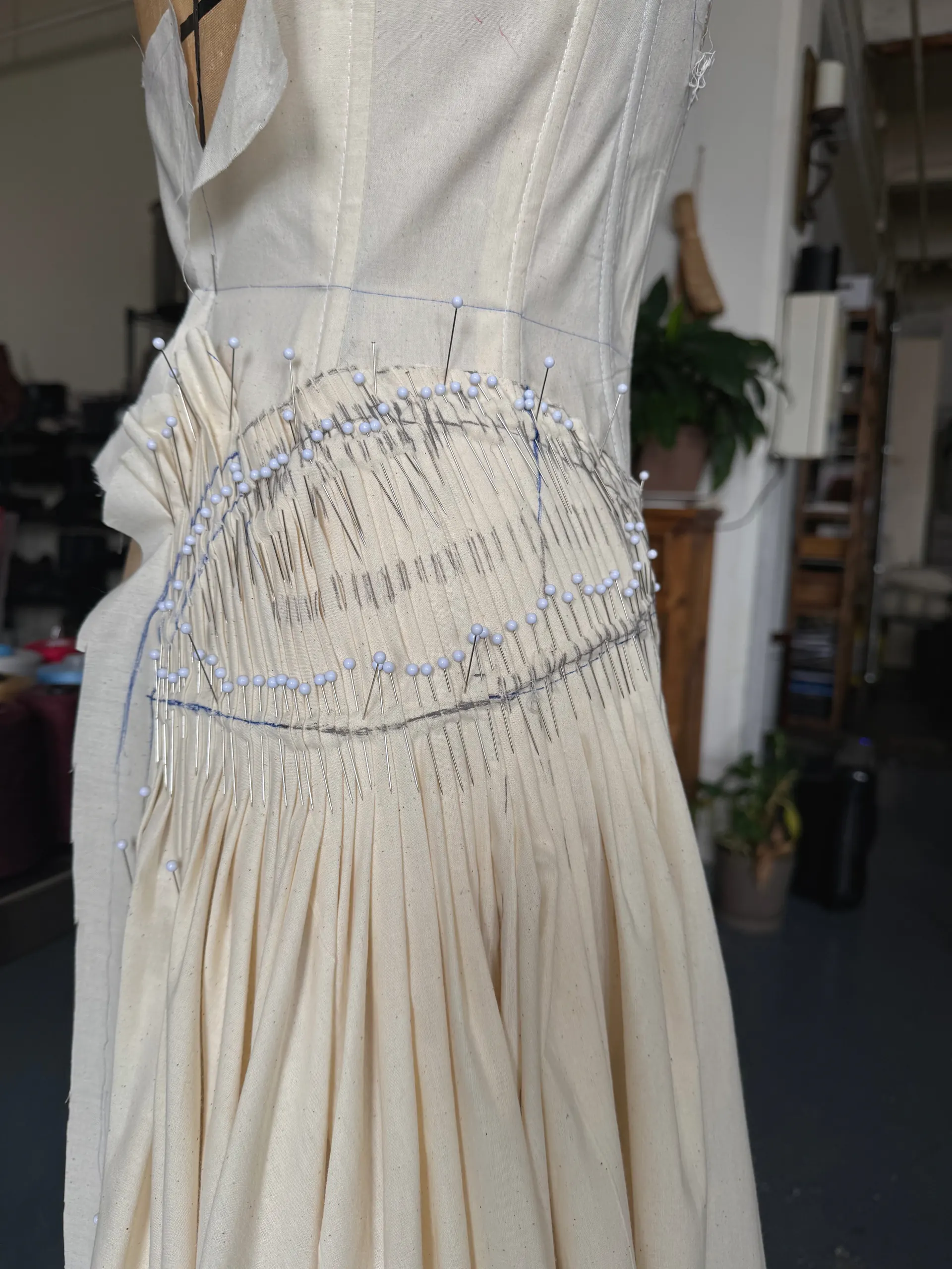 Close view of a pinned, hand-gathered oval hip panel on a cream cotton toile, still on the dress form.