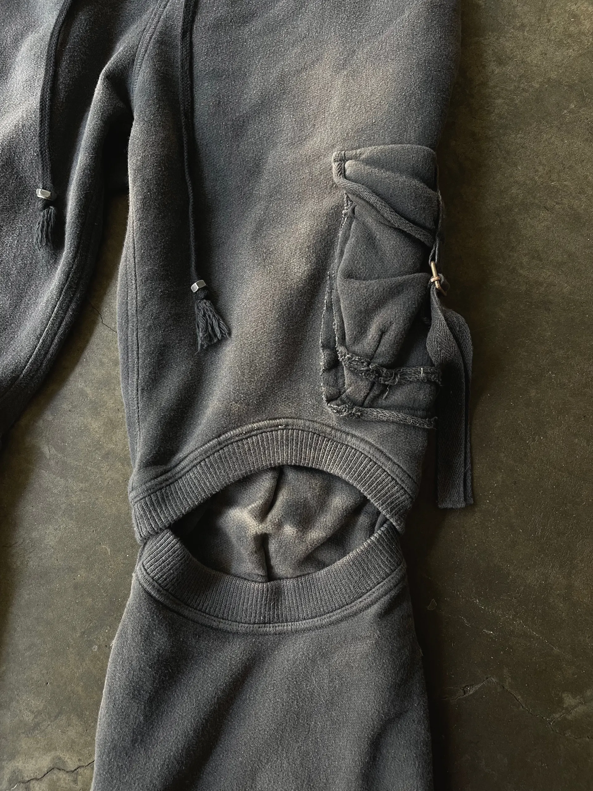 Detail of a fleece cargo trouser leg showing a raw-edged flap pocket, metal-tipped drawcord and a rib-bound knee cut-out.