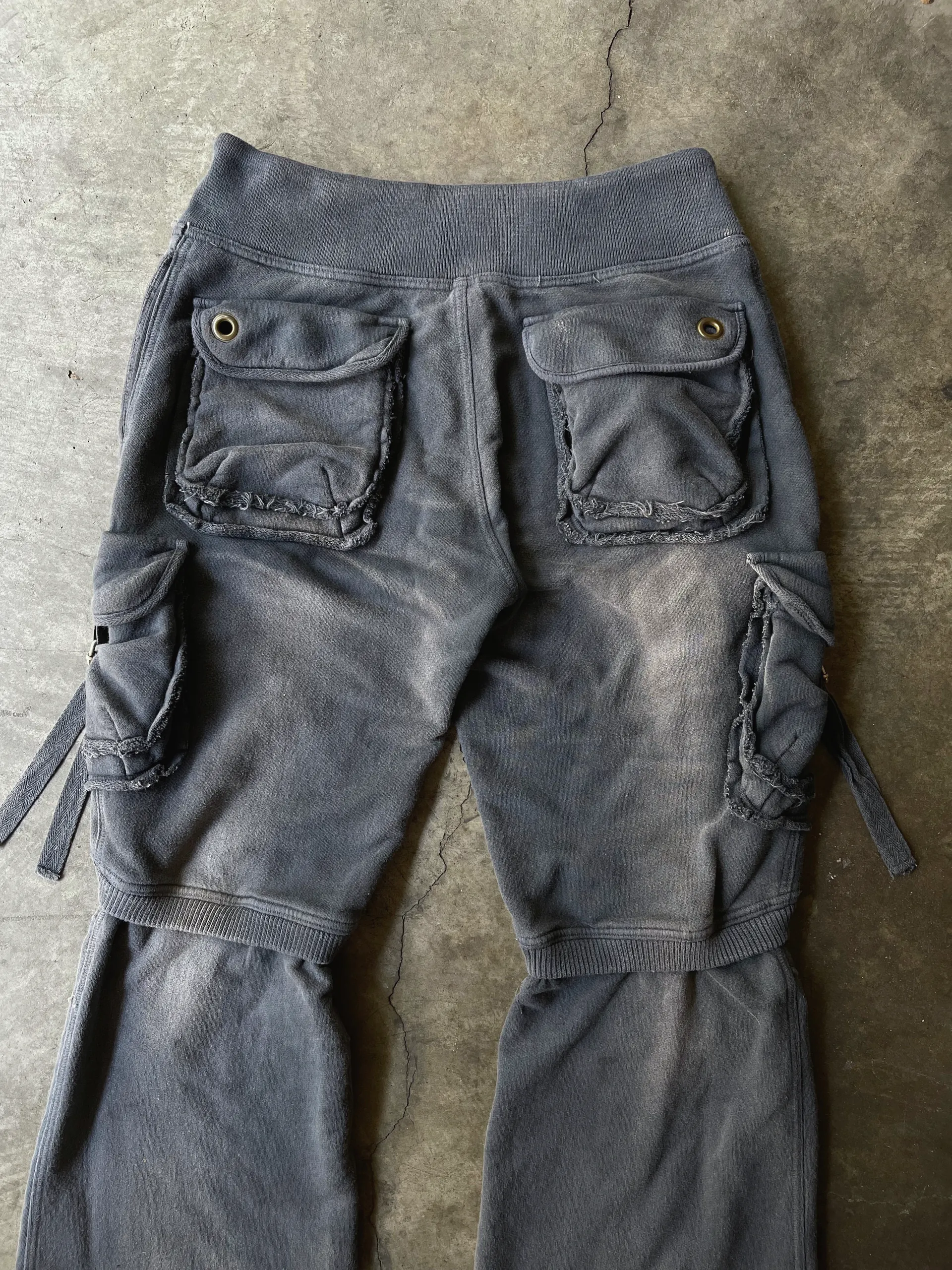 Detail of the back of fleece cargo trousers showing the ribbed waistband, grommeted flap pockets with raw-edged trim and the ribbed leg join.