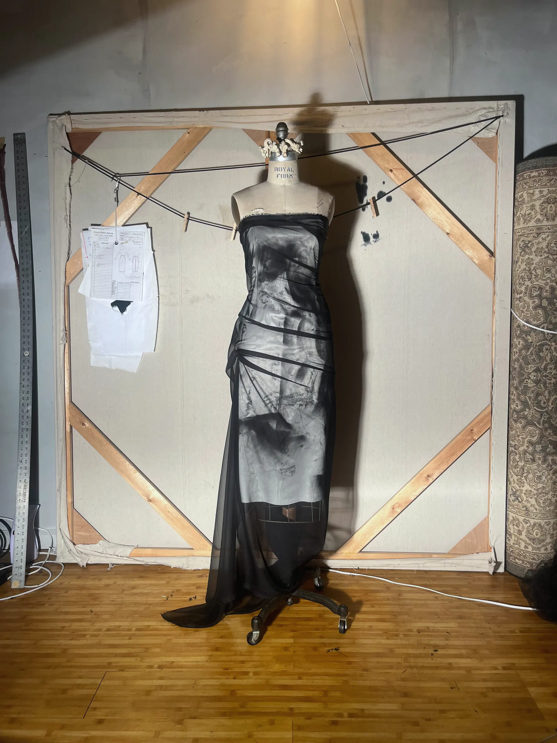 Strapless floor-length gown of sheer black chiffon over a grey printed underlayer, with wrapped waist ties and a trailing hem, on a dress form in the studio.