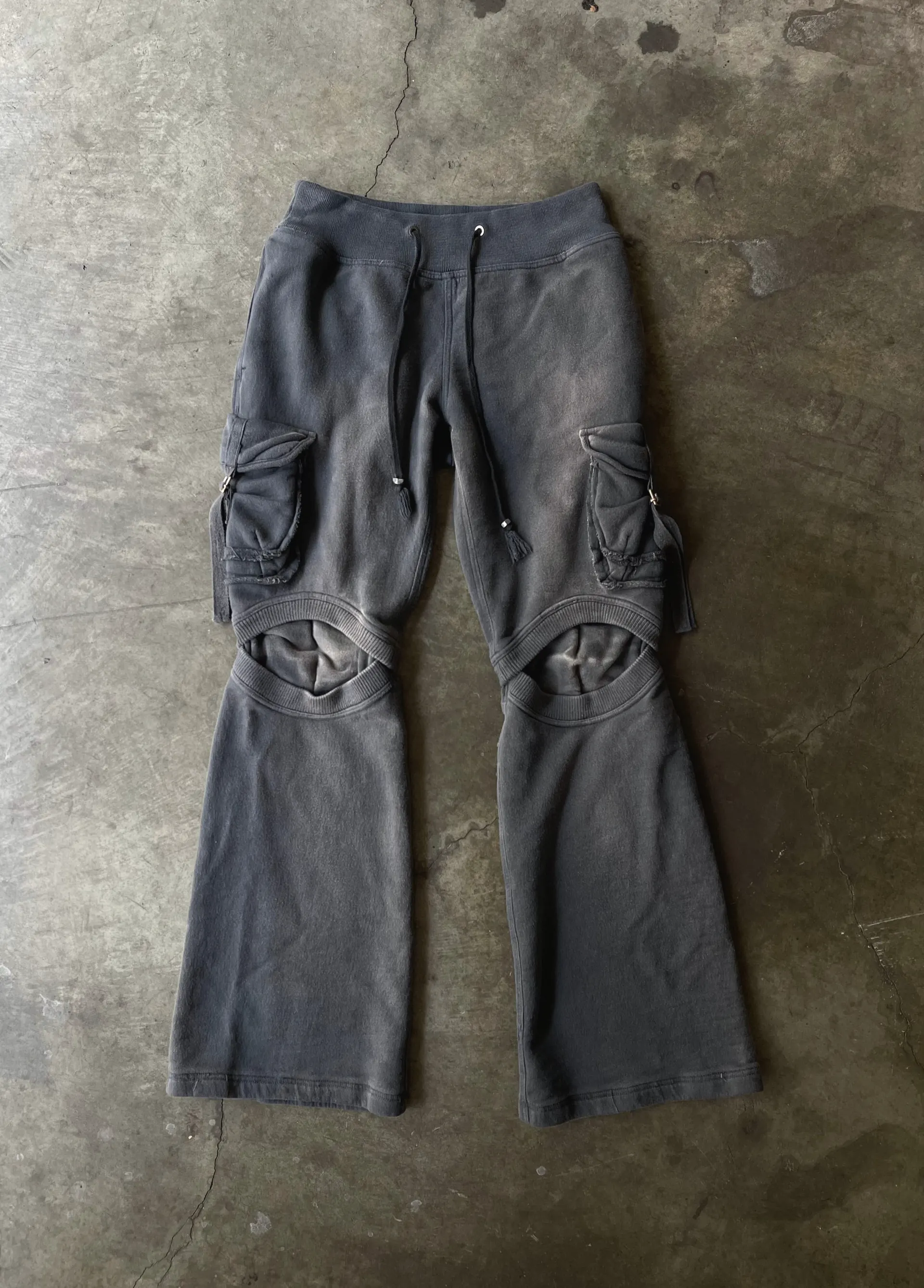 Washed charcoal fleece cargo trousers with drawstring waist, flap cargo pockets and ribbed knee cut-outs, laid flat on concrete.